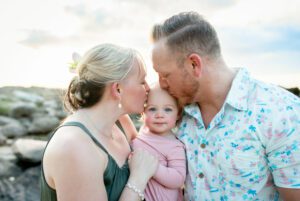 mom and dad kissing baby on side of head